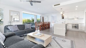 A modern living room with a grey sofa, wooden coffee table, and a dining area with wooden chairs.