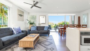 A modern living room with a sofa, coffee table, and a dining area with chairs and a table.