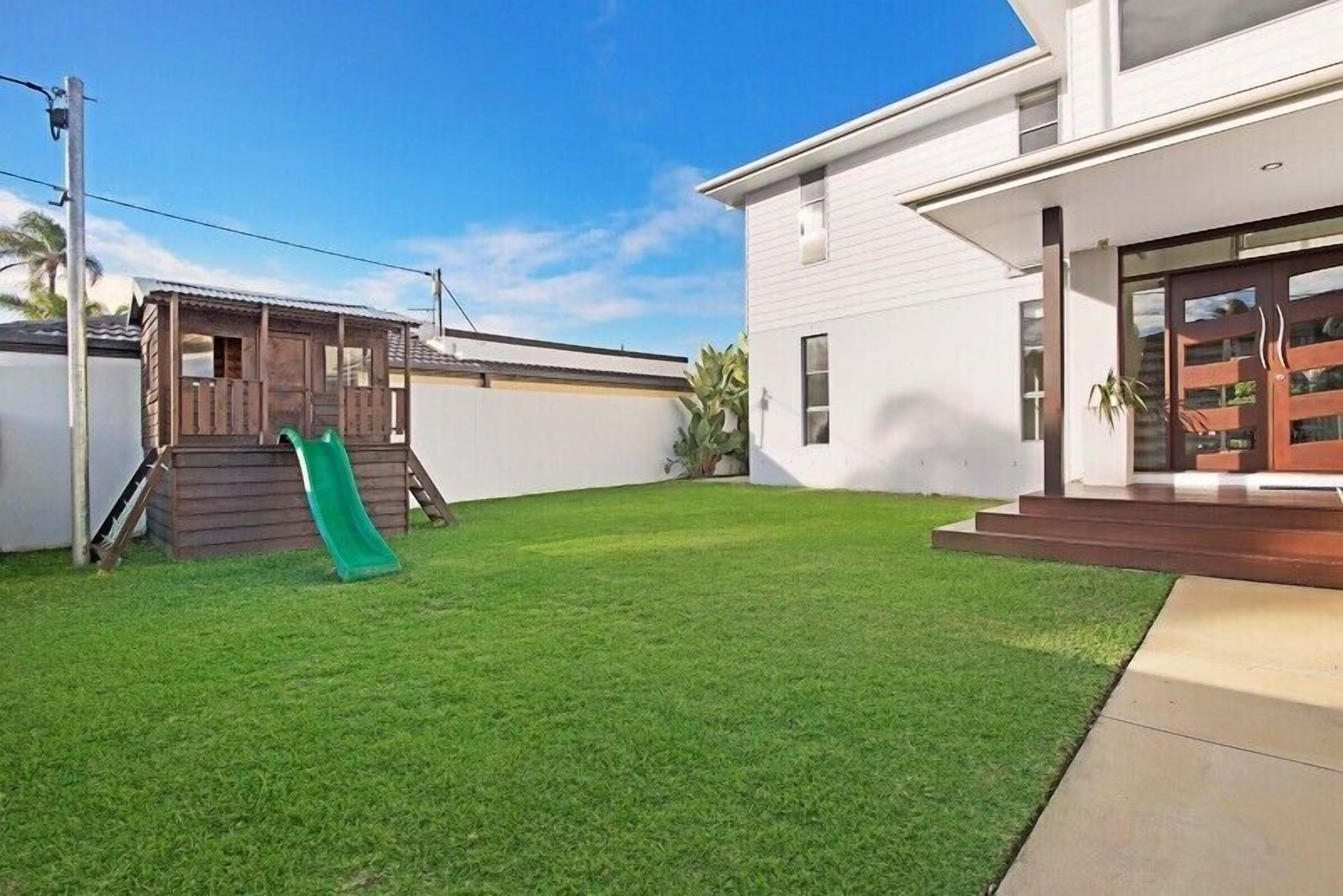 A modern house with a well-maintained lawn, a wooden playhouse, and a green slide.