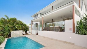 Une maison moderne dotée d’une piscine, de grandes fenêtres et d’un espace extérieur couvert.