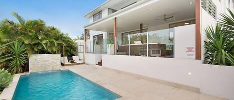 A modern house with a swimming pool, large windows, and a covered outdoor area.