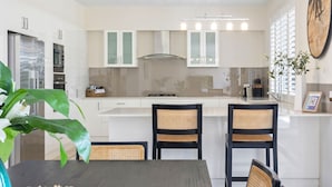 Une cuisine moderne avec des meubles blancs, un îlot central et deux chaises en osier.