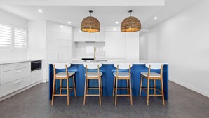A modern kitchen with white cabinets, a blue island, and wooden bar stools.
