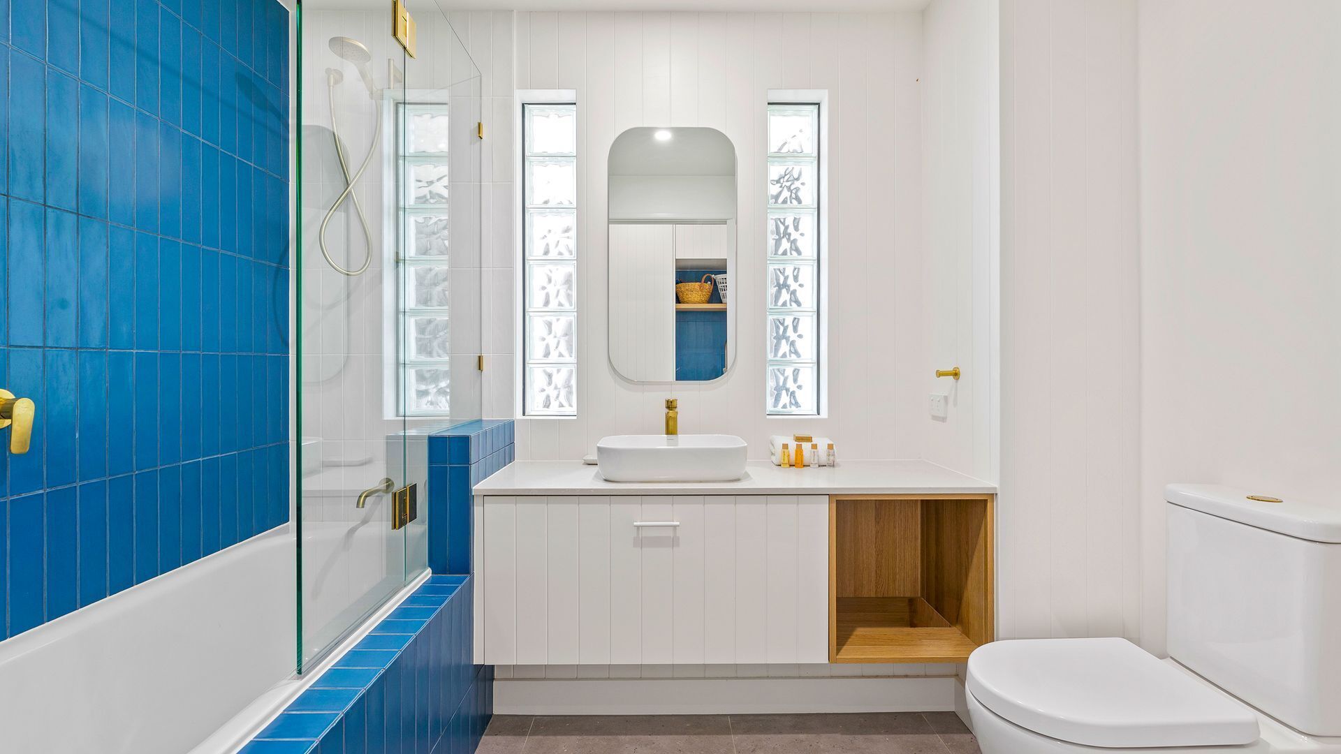 Een badkamer met een douchecabine van glas, een witte wastafel met gouden kraan en een toilet.