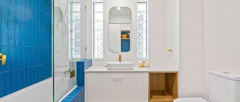 Een badkamer met een douchecabine van glas, een witte wastafel met gouden kraan en een toilet.
