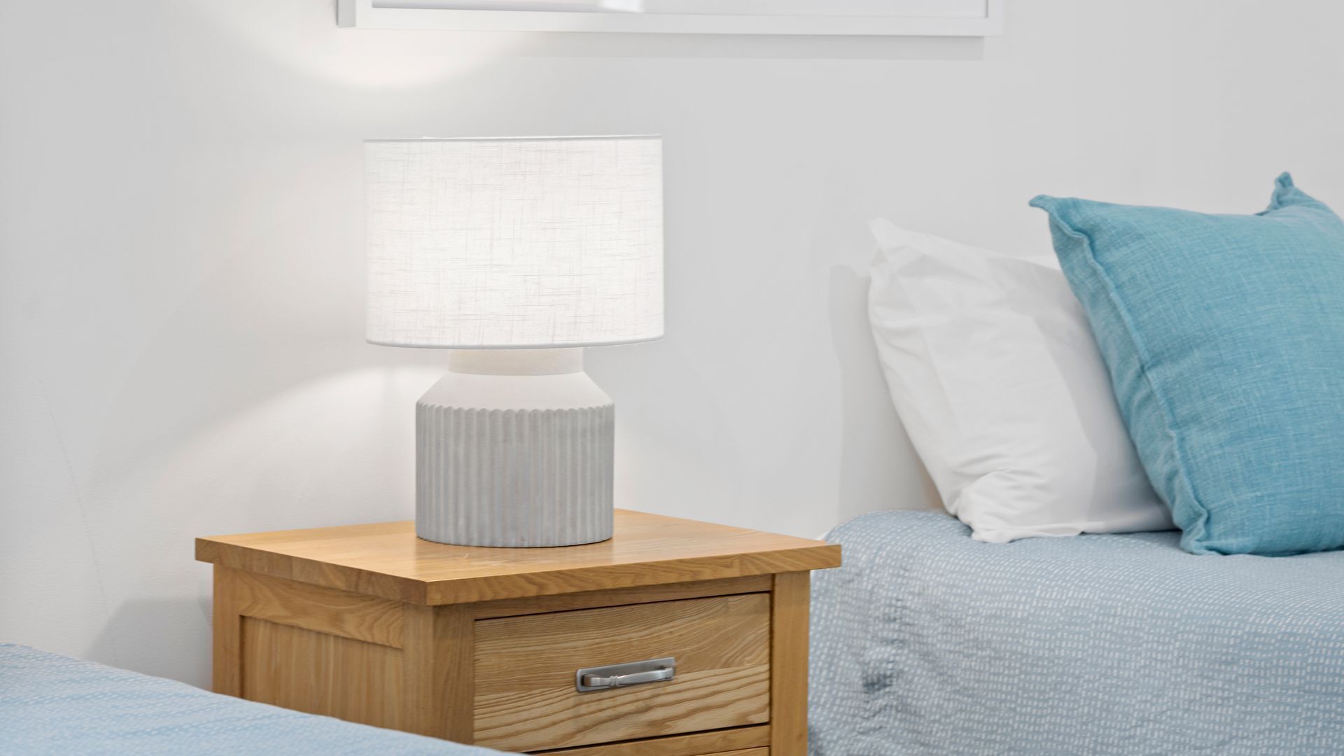A bedside table with a lamp, a drawer, and a bed with pillows.