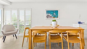 A dining area with a wooden table and chairs, a potted plant, and a framed artwork on the wall.