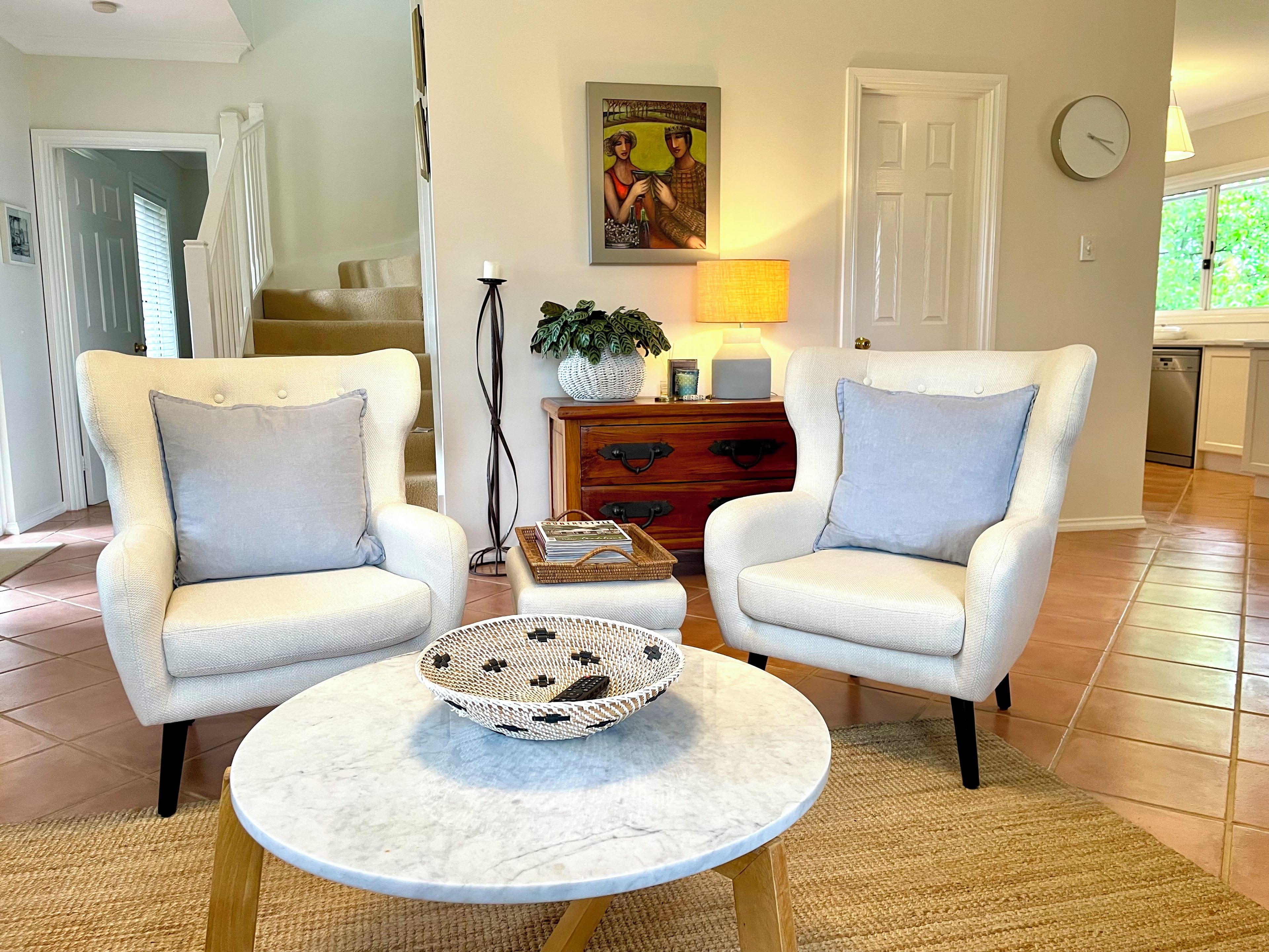 A living room with two armchairs, a coffee table, a lamp, a painting, and a clock on the wall.