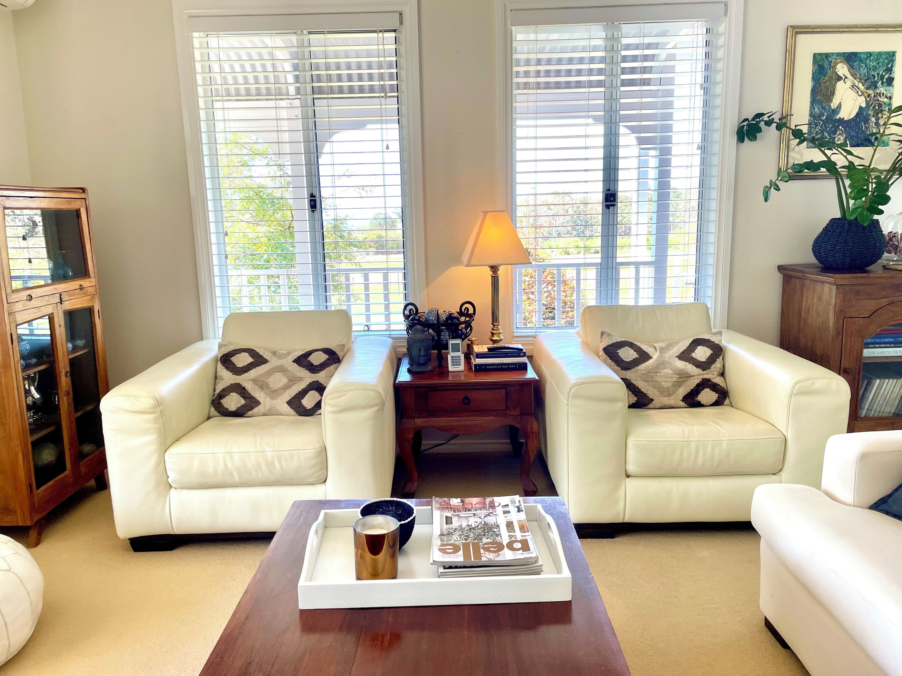 A living room with two white leather sofas, a wooden coffee table with magazines and a glass, and a lamp on a side table.