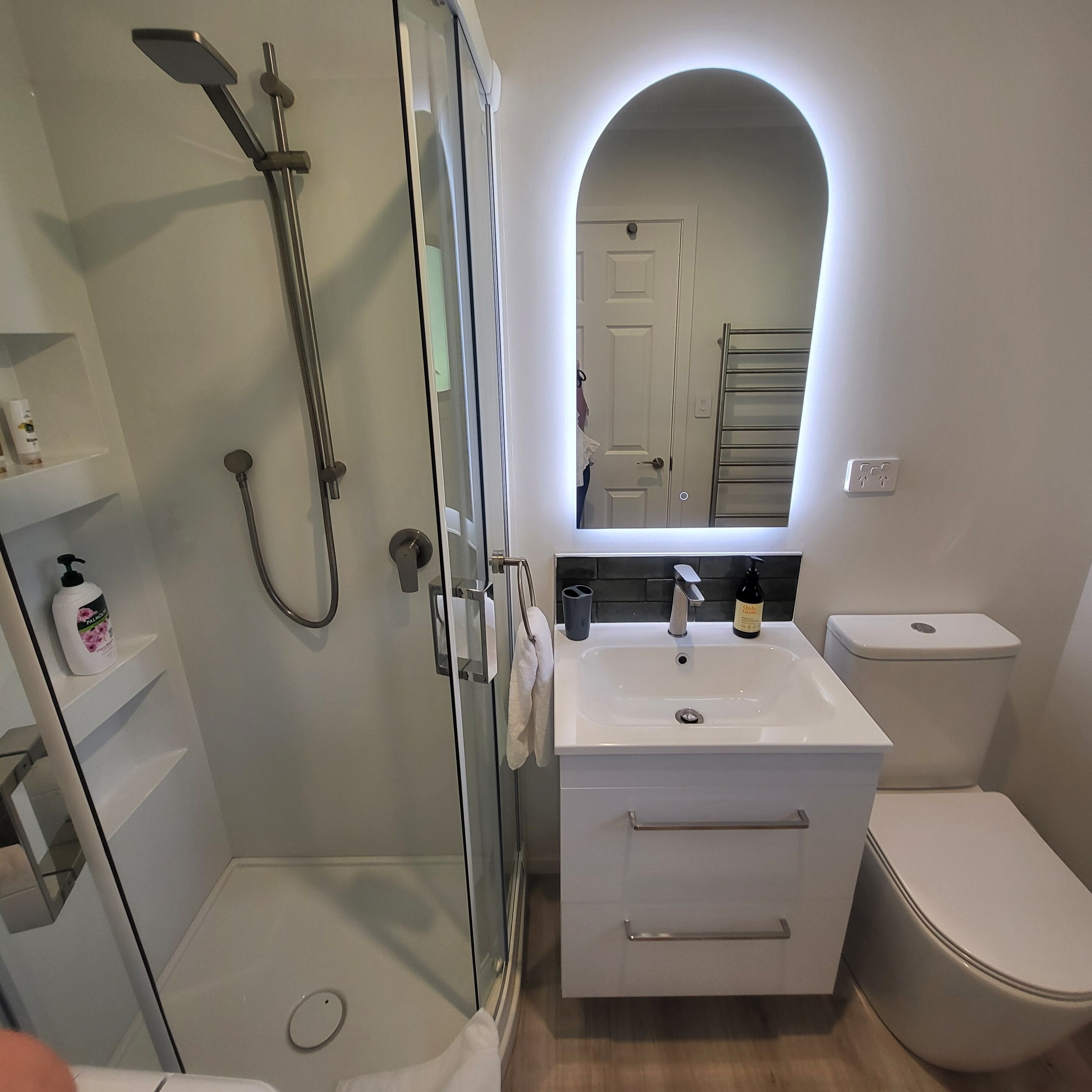 A modern bathroom with a glass-enclosed shower, a white sink with a mirror above, and a toilet.