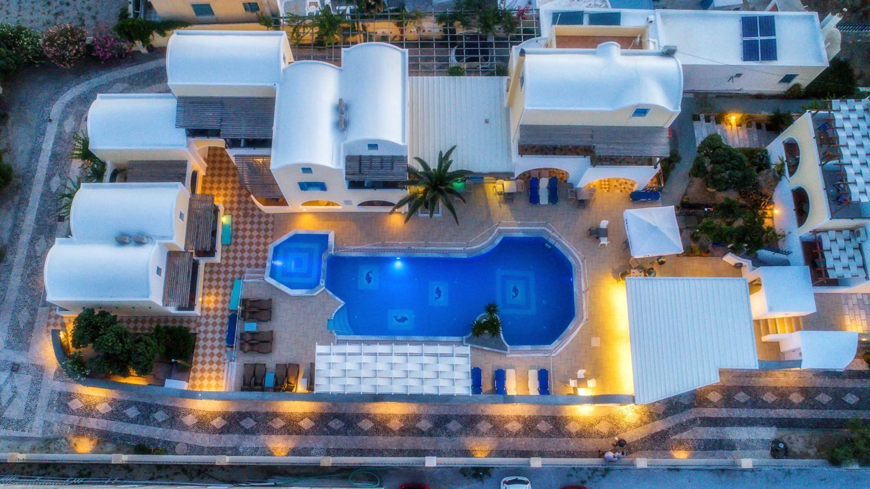 Vista aérea de un resort con piscina central, varias villas y zonas de estar al aire libre.