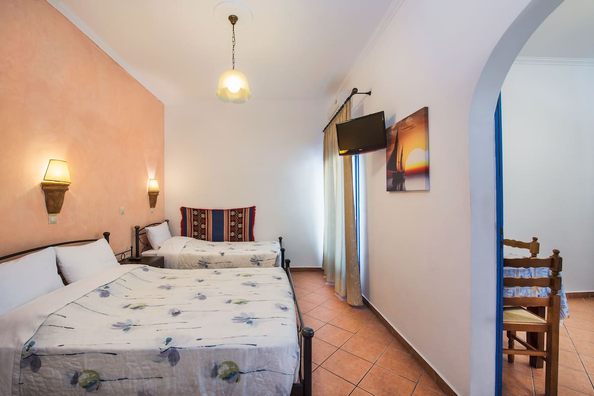 A bedroom with two beds, a television mounted on the wall, and a chair.
