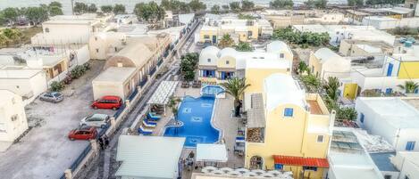 Un pueblo costero con piscina, automóviles estacionados y edificios de arquitectura mediterránea.