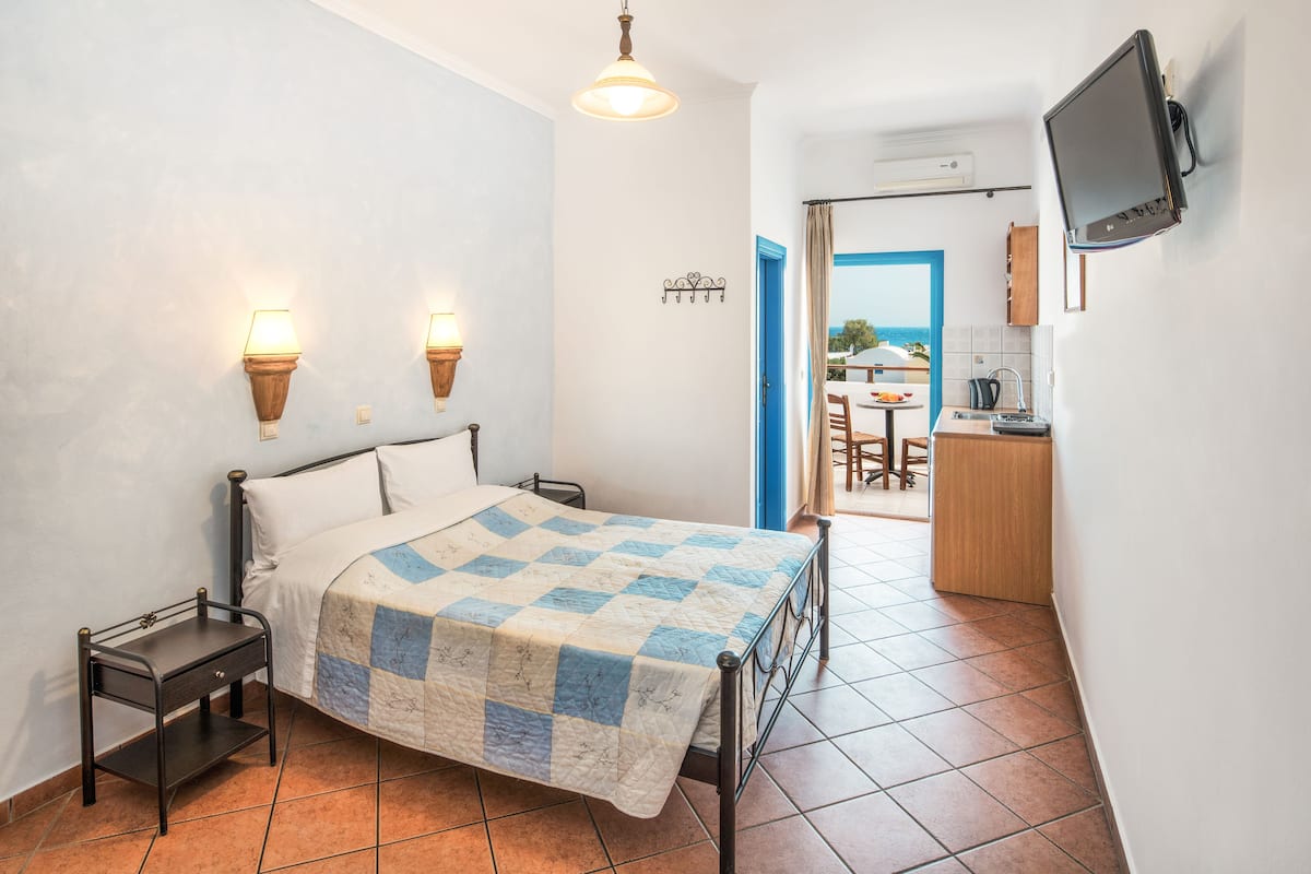 A bedroom with a bed, bedside tables, a wall-mounted TV, and a view into the kitchen.