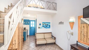 Una escala porta a un dormitori al sostre, una cuina americana, un sofà, un telèfon fixat a la paret i una televisió.