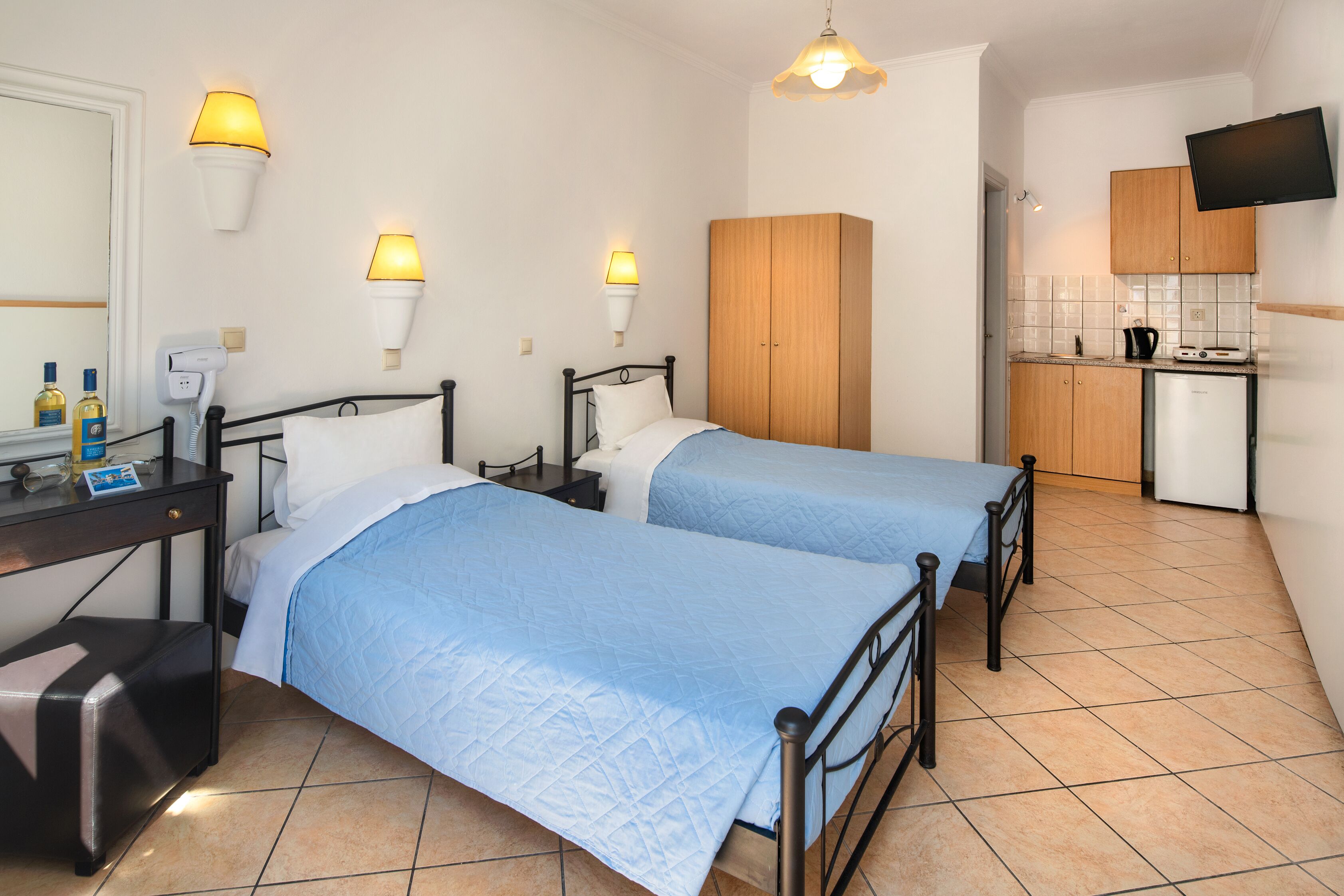 A hotel room with two beds, a desk, a wardrobe, a television, and a kitchenette.