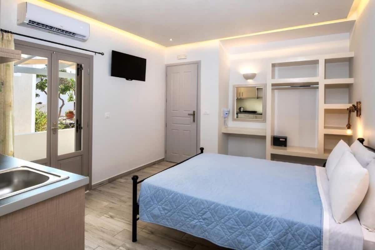 A bedroom with a bed, a built-in wardrobe, a TV, and a window with a view of greenery.