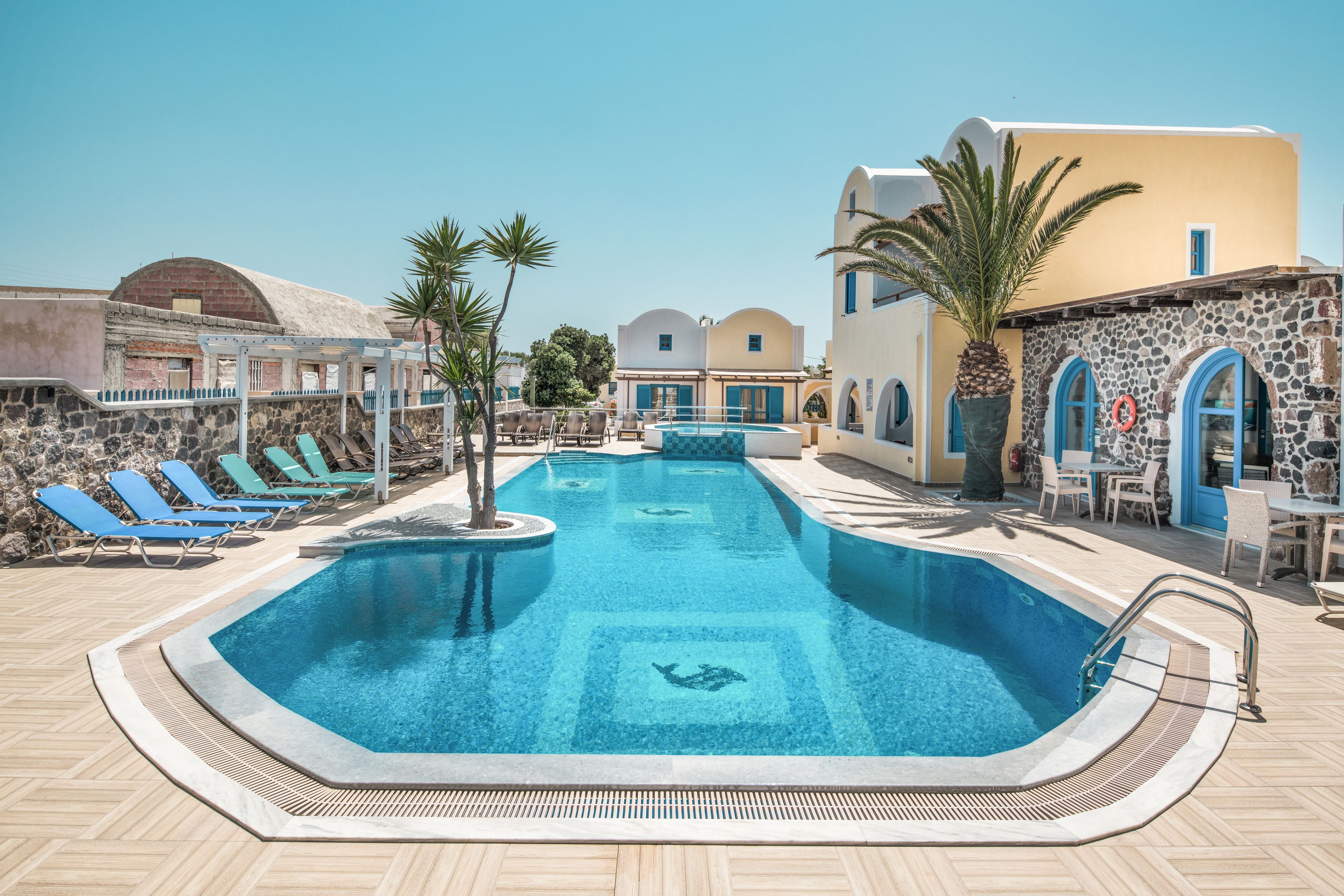 Una piscina con sillas de descanso, un muro de piedra y un edificio con ventanas azules.
