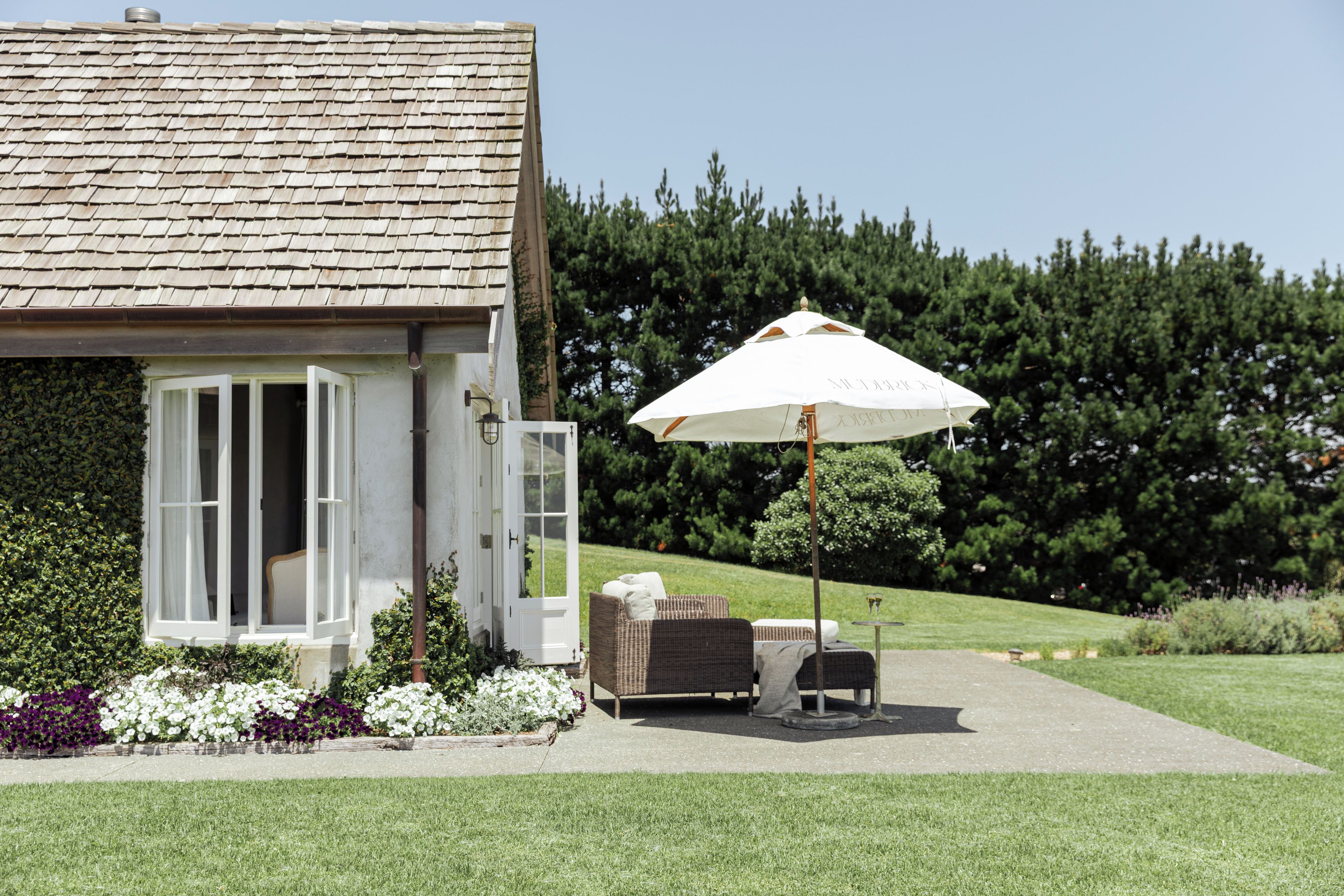 A house with a covered patio area featuring a white umbrella, a wicker sofa, and a small table.