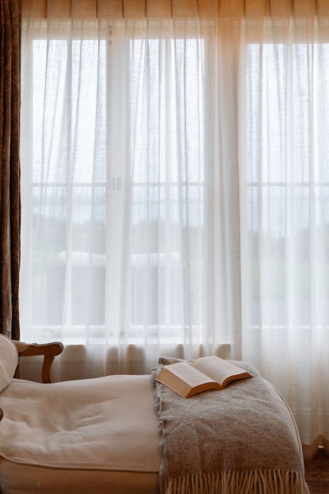 A room with a bed, a chair, and a window with sheer curtains.