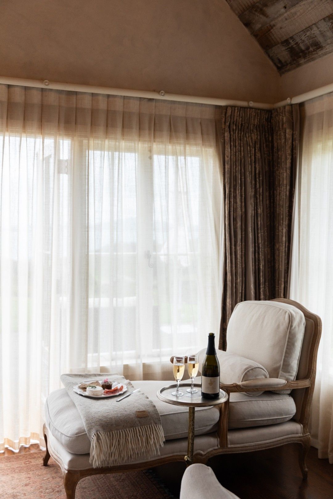 A cozy room with a cushioned seating area, a small round table with a bottle and glasses, and a plate of food.