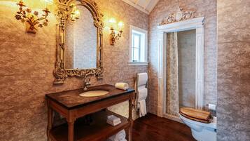 A bathroom with a wooden vanity, a large ornate mirror, wall sconces, a towel rack, and a toilet.