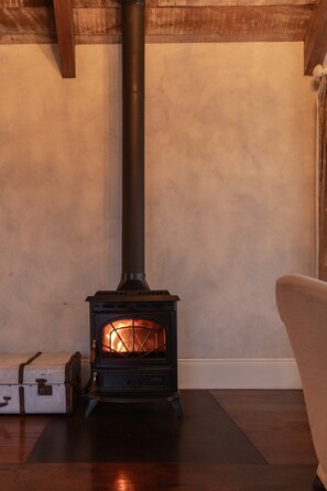 A wood-burning stove with a chimney, placed in a room with wooden flooring and a white wall. - Mudbrick Luxury Cottages (Waiheke Island)