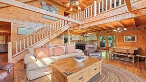 Ein geräumiges Blockhaus-Interieur mit einer zentralen Treppe, einer gemütlichen Sitzecke und einer durchgehenden Tür erkennbaren Küche.