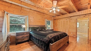 A wooden cabin bedroom with a bed, nightstands, a ceiling fan, and a window with blinds.