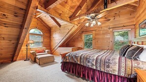 A cozy attic bedroom with a sloped ceiling, wooden beams, a bed with patterned bedding, a chair, and a small table.