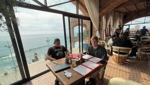 Ein Restaurant mit großen Fenstern mit Meerblick, Holztischlerei und Fliesenboden.