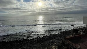 Ein Strand mit Wellen, einer felsigen Küste und einem klaren Himmel mit der Sonne.