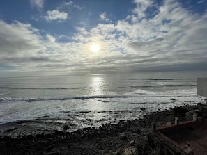 Une plage avec des vagues, une côte rocheuse et un ciel dégagé avec le soleil.