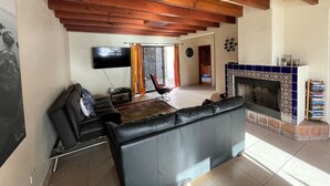Ein Wohnzimmer mit einer schwarzen Ledersofa, einem an der Wand montierten Flachbildfernseher, einem Kamin mit gemusterten Fliesen und einer Holzbalkendecke.
