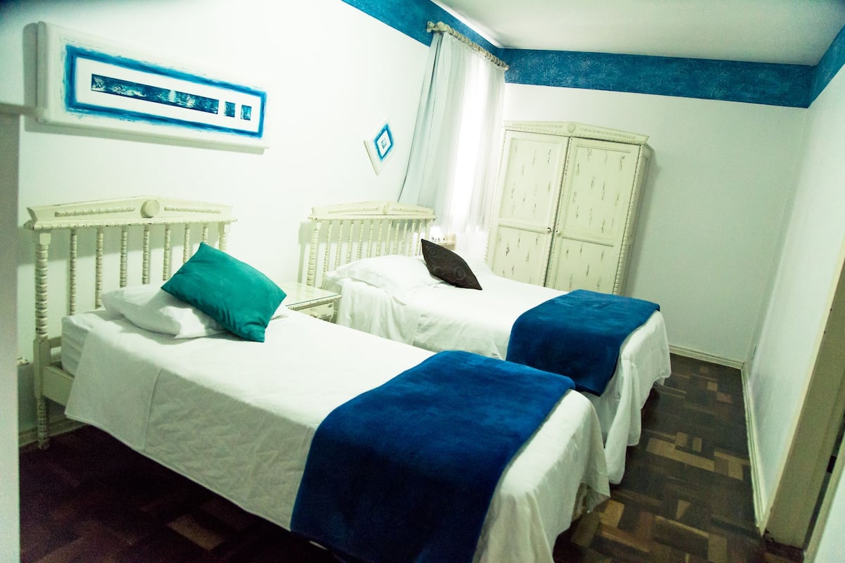 Habitació amb dos llits, cadascun amb un capçal blanc i una manta blava. Hi ha un armari blanc adossat a la paret i una decoració mural blava i blanca.