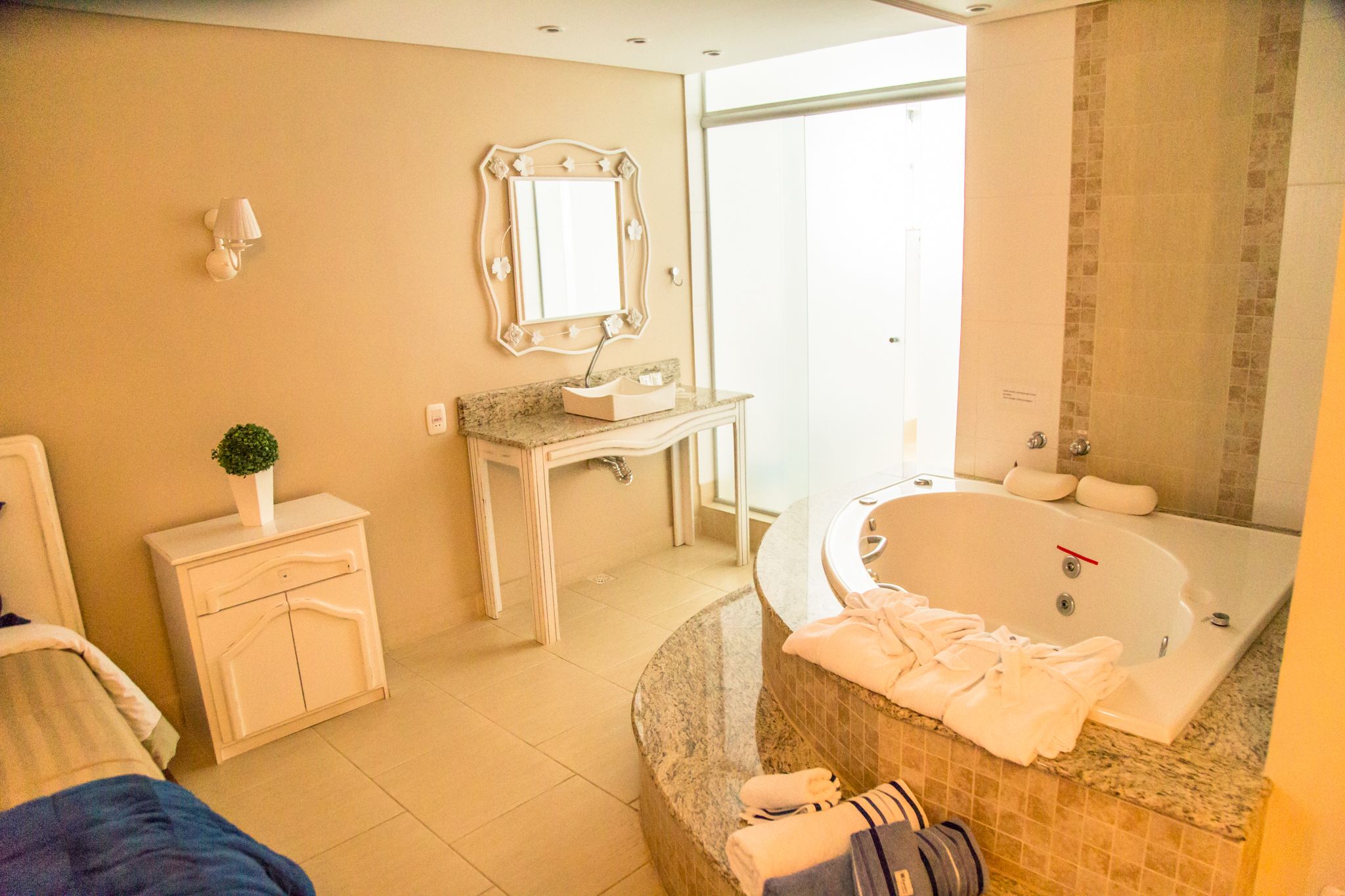 Un baño moderno con una bañera grande, un tocador con espejo, un mueble pequeño y una planta en maceta.