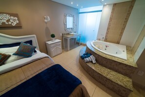 A bedroom with a bed, a bedside table, a nightstand, and a bathroom with a bathtub, sink, and mirror.