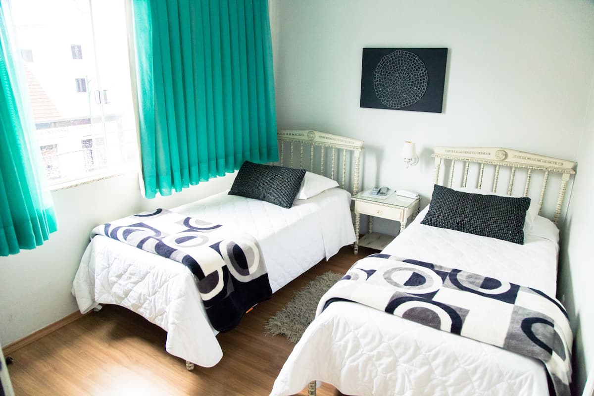 Habitació d'hotel amb dos llits individuals, una finestra amb cortines, una taula de nit amb una làmpada i una obra d'art a la paret.