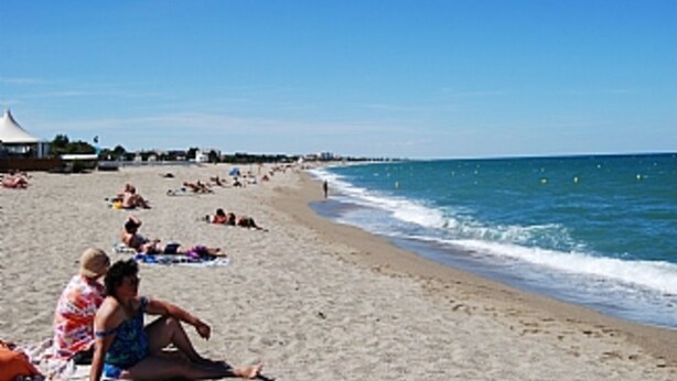 A beach with people sunbathing and swimming.