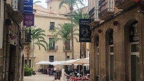 Un vicolo stretto con tavoli all'aperto, palme e edifici con balconi.