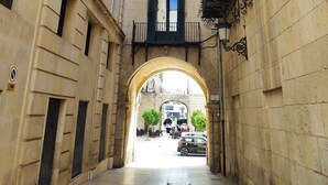 Un stretto vicolo con una torre dell'orologio, edifici in pietra e un arco che conduce a una piazza.