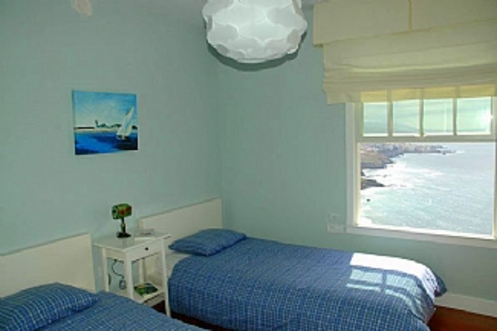 Ein Zimmer mit zwei Betten, einem kleinen Nachttisch mit Lampe, einem Bild von einem Segelboot und einem Fenster mit Meerblick.