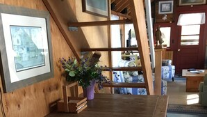 Une table à manger en bois avec des bancs, un vase violet rempli de fleurs et des tableaux encadrés accrochés au mur.