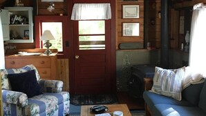 Une pièce mansardée chaleureuse avec un plafond en bois, un ventilateur de plafond, une cheminée, une table en bois, un canapé et un fauteuil.