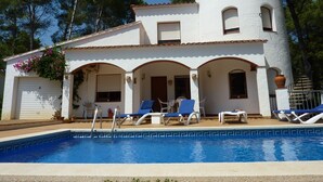 Eine weiße Villa mit Pool und blauen Liegestühlen.