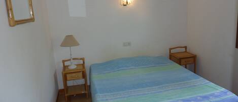 A bedroom with a bed, a nightstand with a lamp, a wall-mounted light, and a small wooden chair.