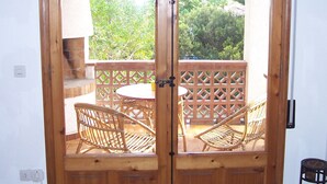 Eine Holztür mit Fensterglas, die auf eine Terrasse mit Korbmöbeln und einem Tisch führt.