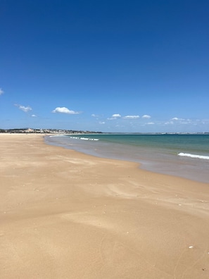 A beach with clear skies, a sandy shore, and a distant shoreline with buildings.