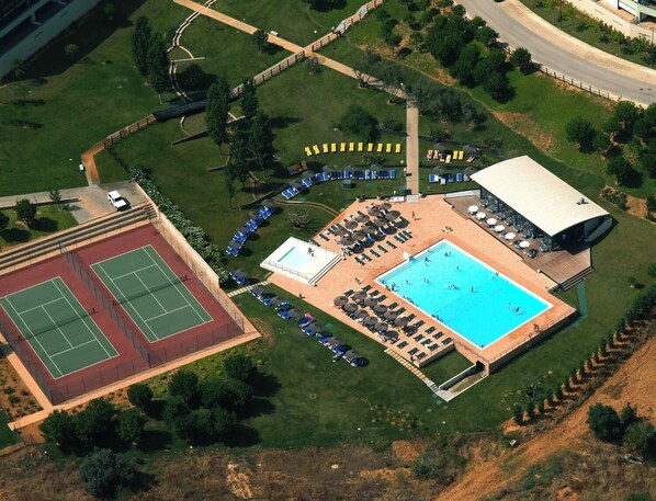 An aerial view of a resort with a swimming pool, tennis courts, and a covered seating area.