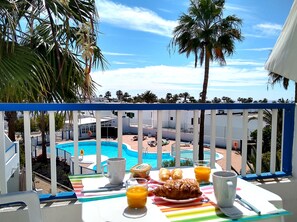 A balcony with a view of a swimming pool, a table with breakfast items, and a white railing. - cosy appartment in a residencial development near the sea (Puerto del Carmen)